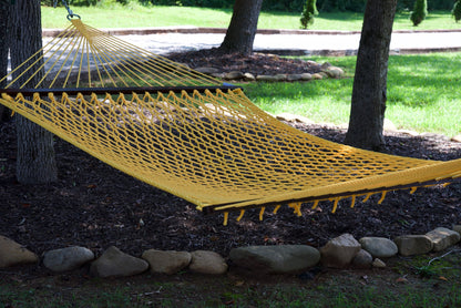 Yellow Jumbo Rope Hammock hanging between two trees in a landscaped backyard.