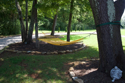Yellow Jumbo Rope Hammock hanging between two trees in a landscaped backyard.