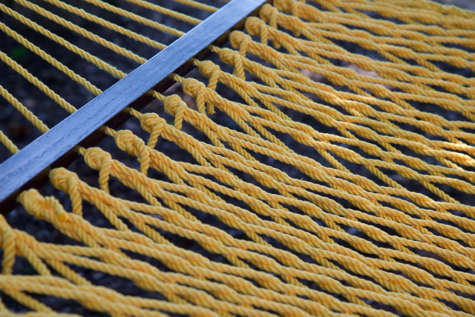 Close view of the varnished wood spreader bar and Yellow polyester rope of the Jumbo Rope Hammock.