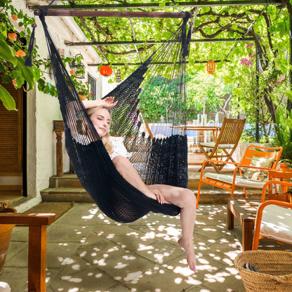 Woman seated in a black Large Caribbean Hammock Chair on a shaded patio under a vine-covered pergola