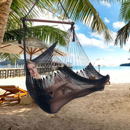 Woman lying back in a black Large Caribbean Hammock Chair on a tropical beach with loungers and palm fronds