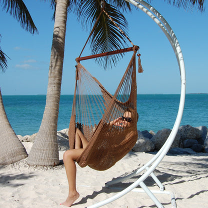 Woman relaxing in a mocha Large Caribbean Hammock Chair on a white arc stand beneath palm trees by the ocean