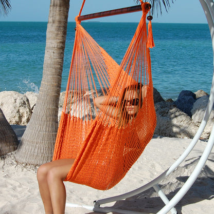 Woman seated in an orange Large Caribbean Hammock Chair on a white arc stand on a sandy beach