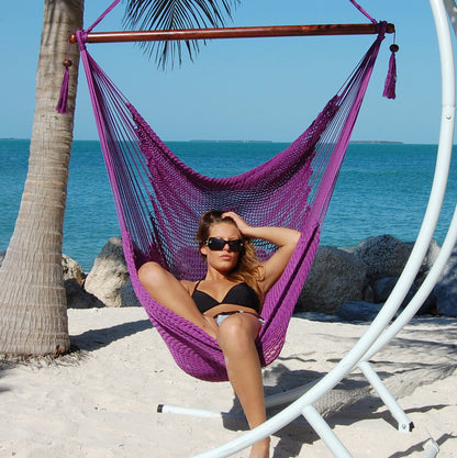 Woman seated in a purple Large Caribbean Hammock Chair on a white arc stand on a sandy beach