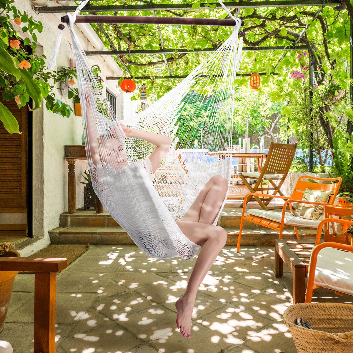 Woman seated in a white Large Caribbean Hammock Chair on a shaded patio under a vine-covered pergola