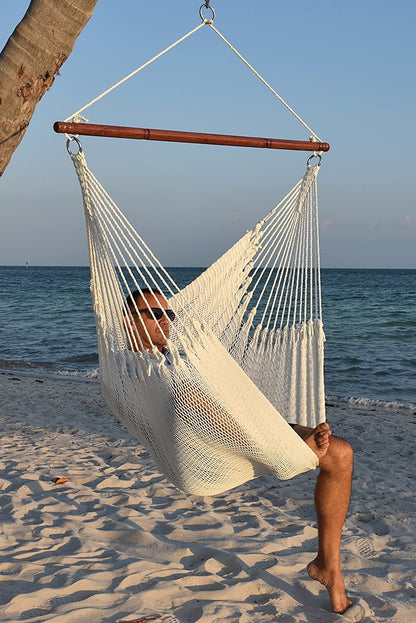 a man sittting in a white caribbean style hammock chair at the beach