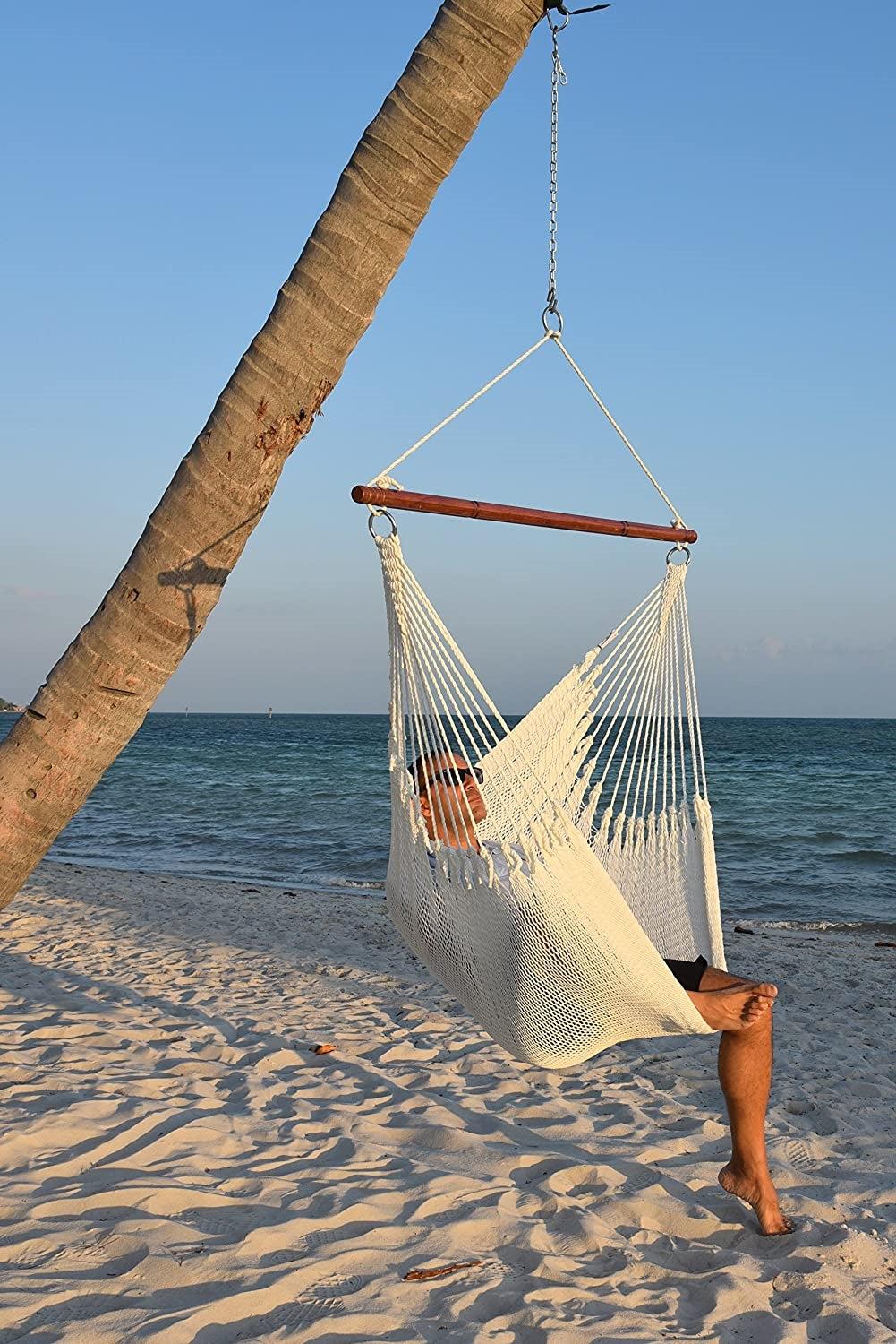 a man sitting in a white hammock chair that is hanging from a coconut tree