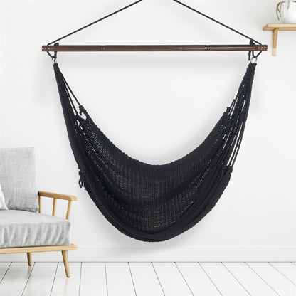 Black Jumbo Caribbean Hammock Chair hanging indoors beside a pale wood armchair against a white wall
