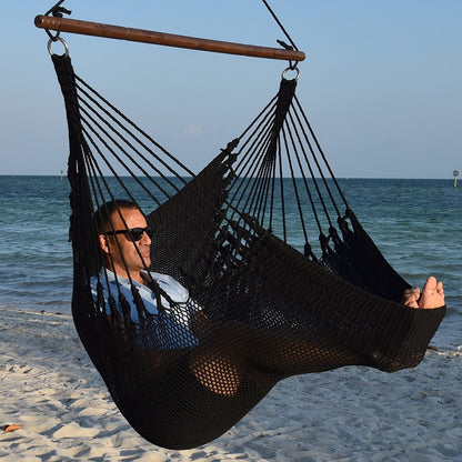 Man in sunglasses stretched out in a black Jumbo Caribbean Hammock Chair with calm ocean behind