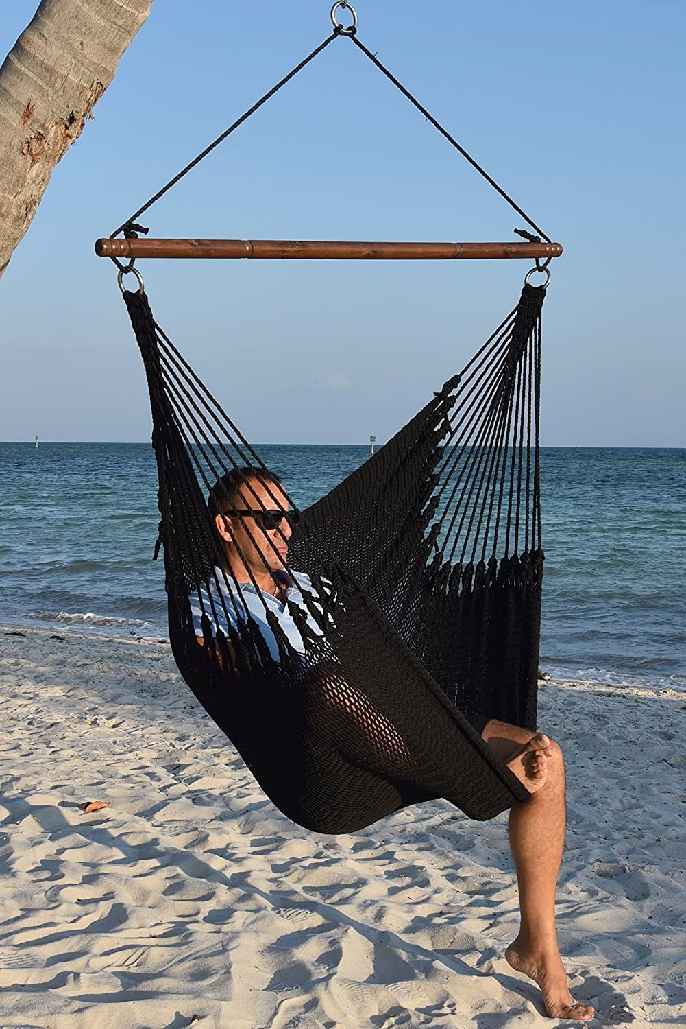 Man in sunglasses seated in a black Jumbo Caribbean Hammock Chair on a white sand beach