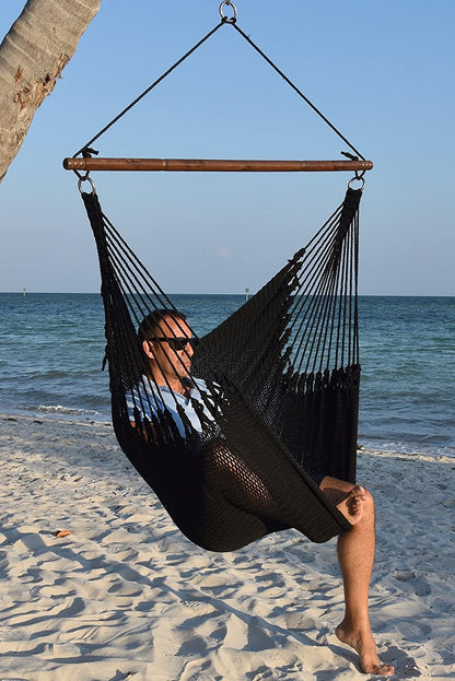 Man in sunglasses seated in a black Jumbo Caribbean Hammock Chair on a white sand beach