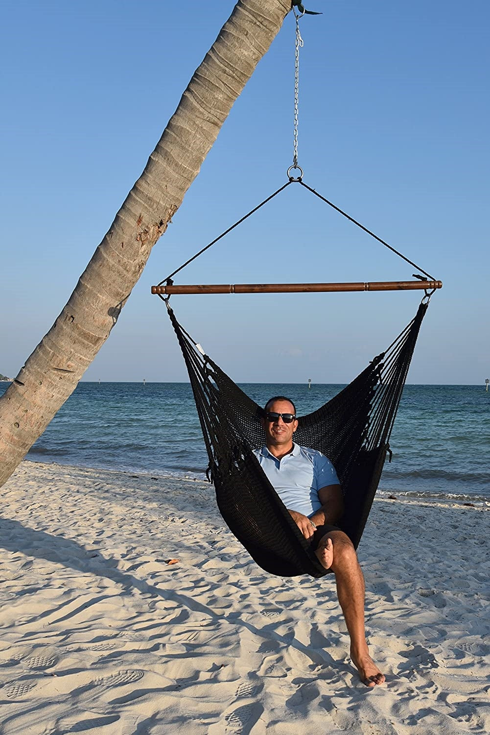 Man relaxing in a black Jumbo Caribbean Hammock Chair hung from a leaning palm tree on a beach