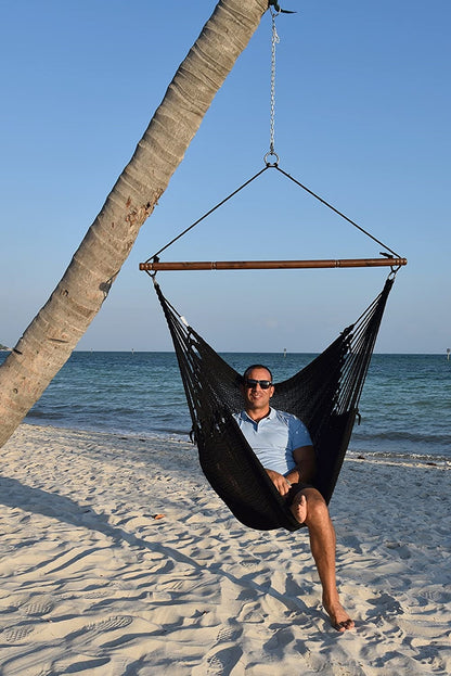 Man relaxing in a black Jumbo Caribbean Hammock Chair hung from a leaning palm tree on a beach