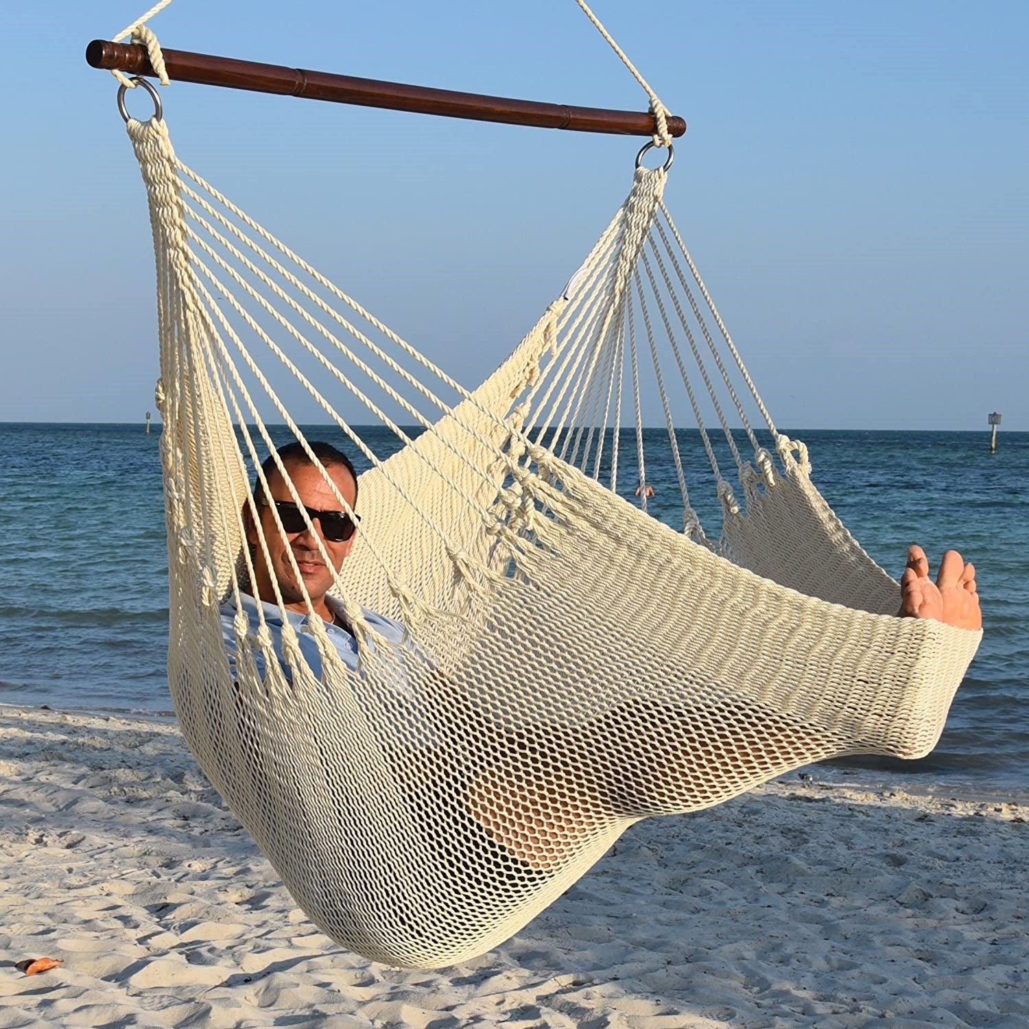 Man in sunglasses stretched out in a cream Jumbo Caribbean Hammock Chair with calm ocean behind