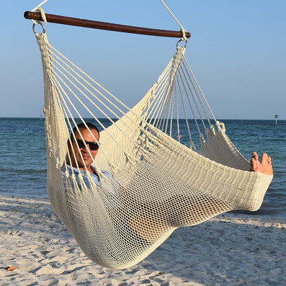 Man in sunglasses stretched out in a cream Jumbo Caribbean Hammock Chair with calm ocean behind
