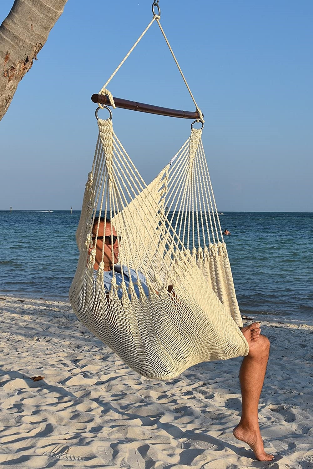 Man in sunglasses seated in a cream Jumbo Caribbean Hammock Chair on a white sand beach