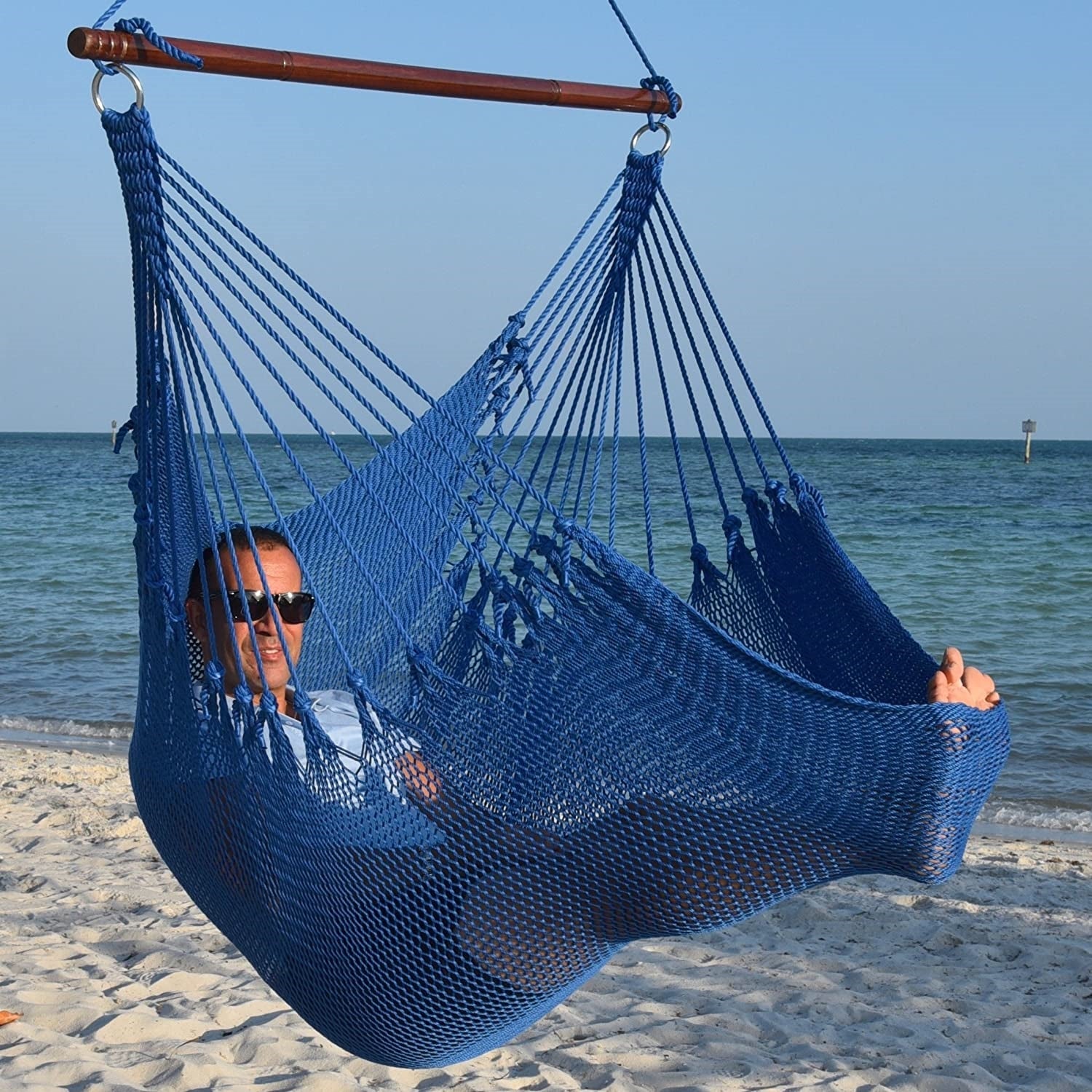 Man in sunglasses stretched out in a dark blue Jumbo Caribbean Hammock Chair with calm ocean behind