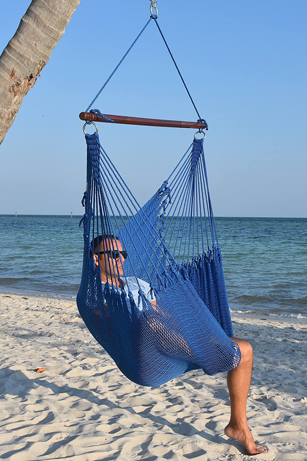 Man in sunglasses seated in a dark blue Jumbo Caribbean Hammock Chair on a white sand beach