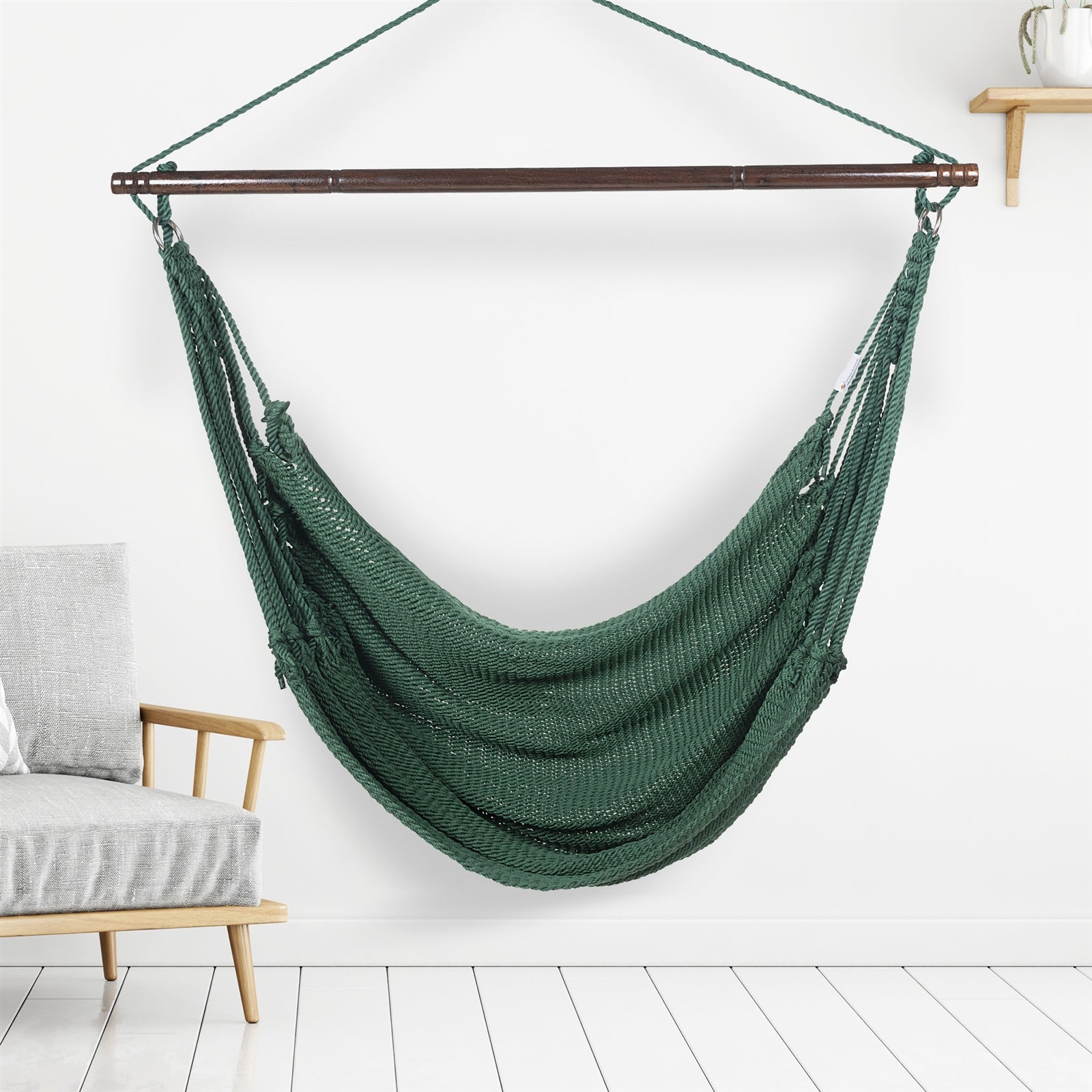 Green Jumbo Caribbean Hammock Chair hanging indoors beside a pale wood armchair against a white wall
