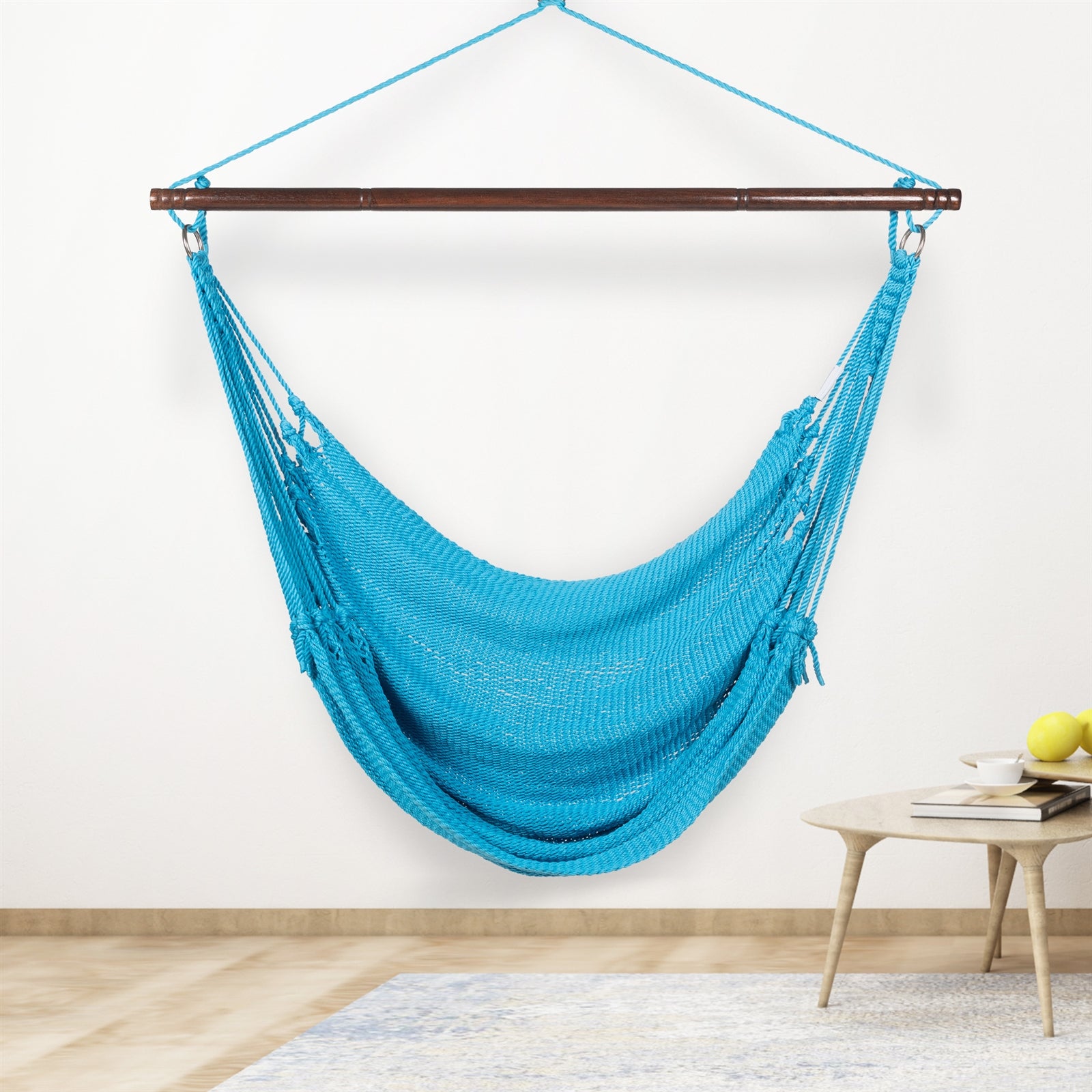 Light blue Jumbo Caribbean Hammock Chair hanging indoors beside a small round side table against a cream wall