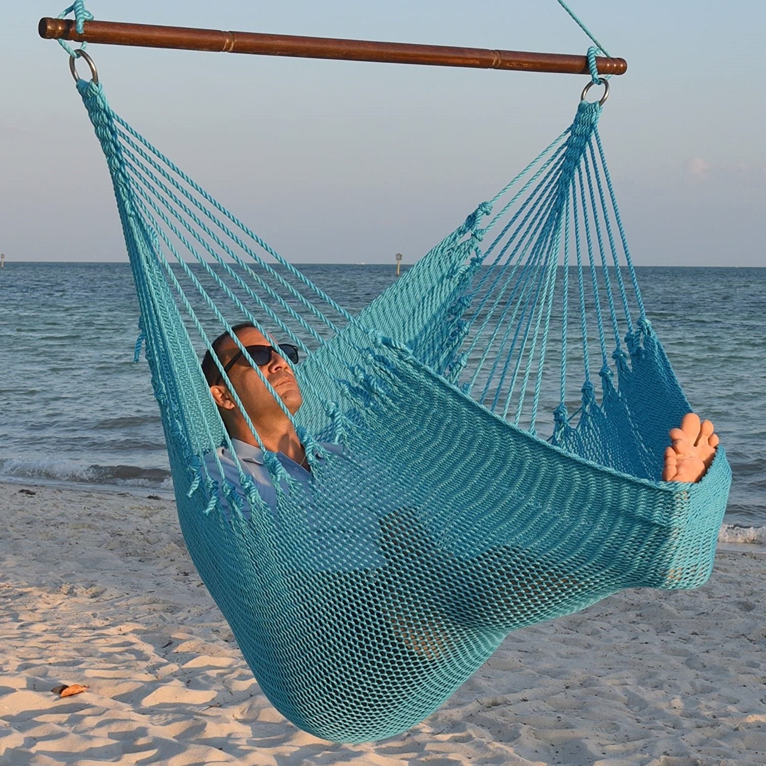 Man in sunglasses stretched out in a light blue Jumbo Caribbean Hammock Chair with calm ocean behind
