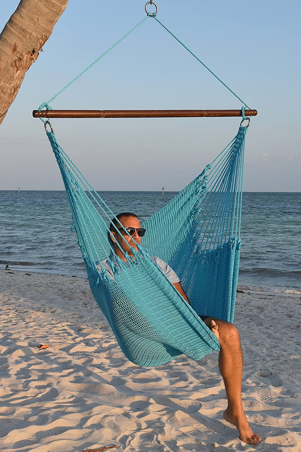 Man in sunglasses seated in a light blue Jumbo Caribbean Hammock Chair on a white sand beach
