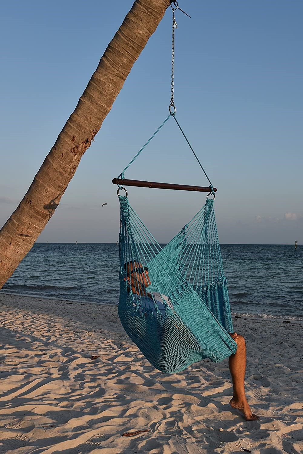 Man relaxing in a light blue Jumbo Caribbean Hammock Chair hung from a leaning palm tree on a beach