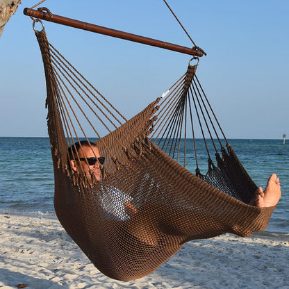 Man in sunglasses stretched out in a mocha Jumbo Caribbean Hammock Chair with calm ocean behind