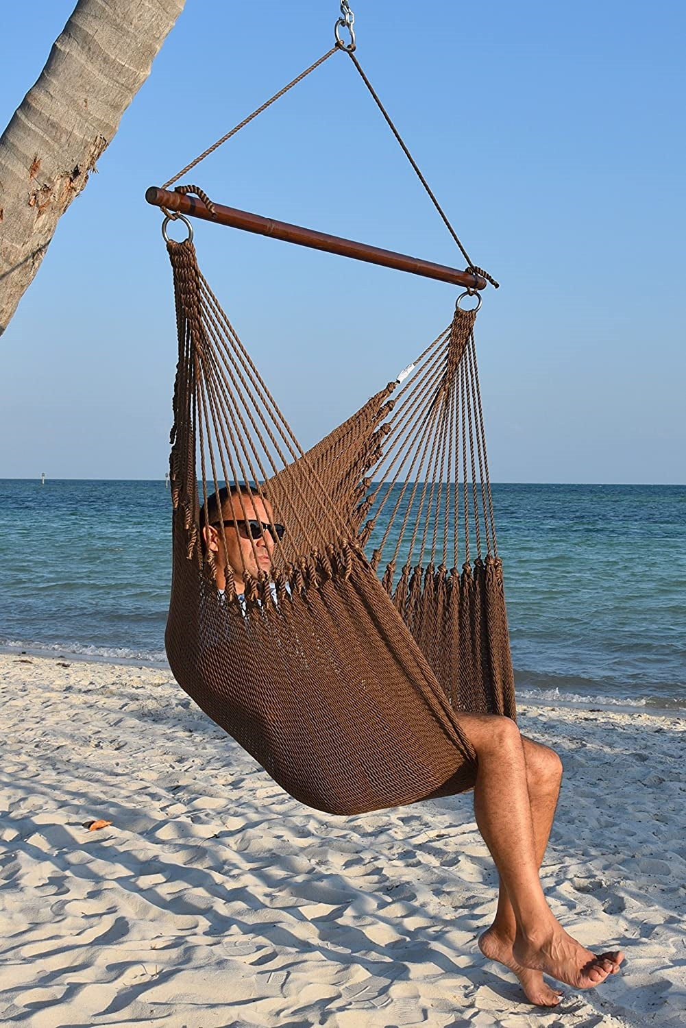 Man in sunglasses seated in a mocha Jumbo Caribbean Hammock Chair on a white sand beach