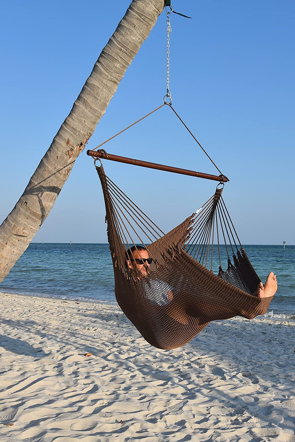 Man relaxing in a mocha Jumbo Caribbean Hammock Chair hung from a leaning palm tree on a beach