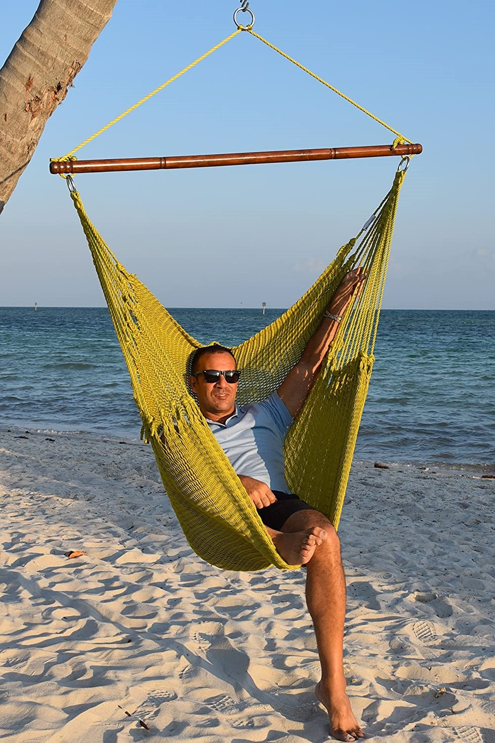 Man in sunglasses seated in an olive Jumbo Caribbean Hammock Chair on a white sand beach