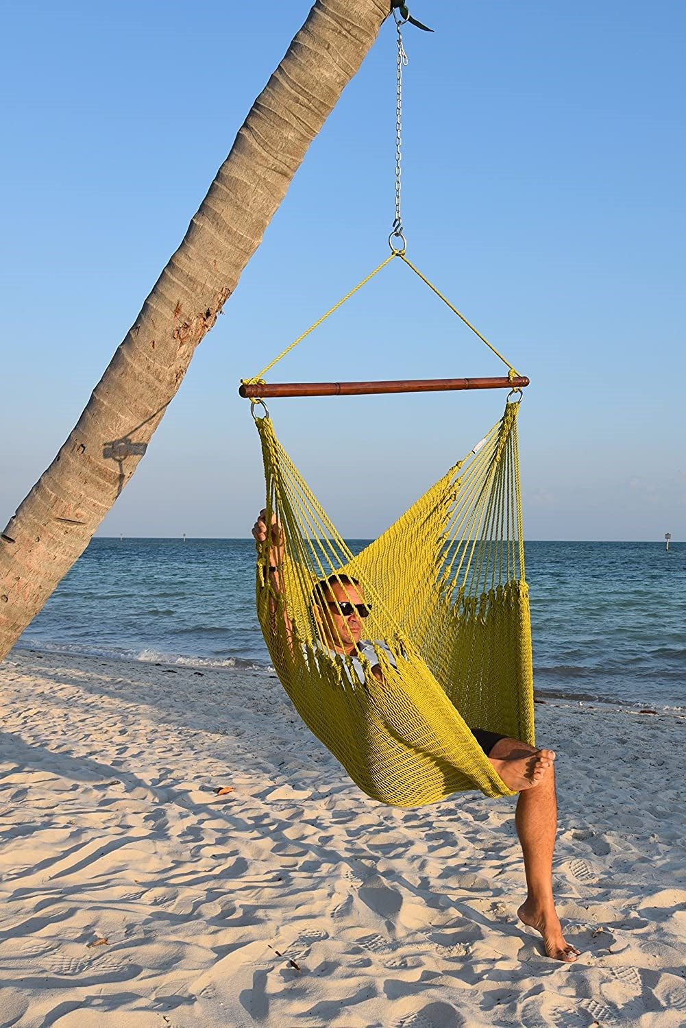 Man relaxing in an olive Jumbo Caribbean Hammock Chair hung from a leaning palm tree on a beach