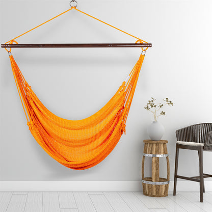 Orange Jumbo Caribbean Hammock Chair hanging beside a barrel side table and rattan stool against a pale grey wall