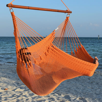 Man in sunglasses stretched out in an orange Jumbo Caribbean Hammock Chair with calm ocean behind
