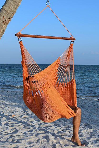Man in sunglasses seated in an orange Jumbo Caribbean Hammock Chair on a white sand beach