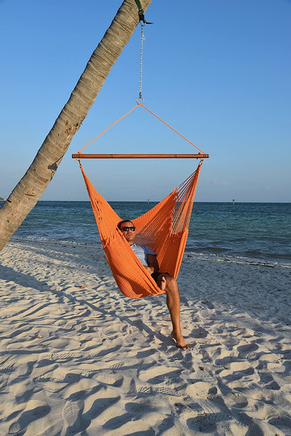 Man relaxing in an orange Jumbo Caribbean Hammock Chair hung from a leaning palm tree on a beach