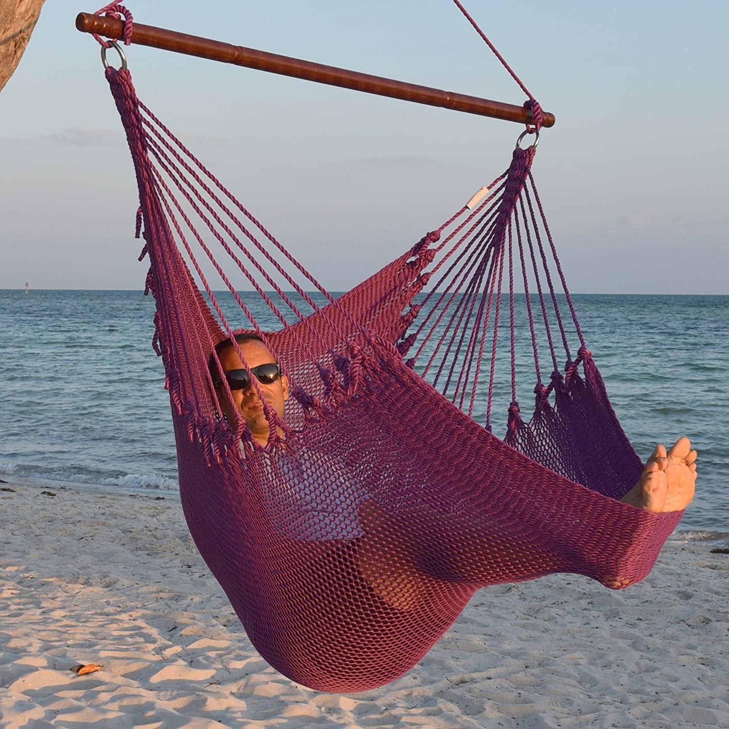 Man in sunglasses stretched out in a purple Jumbo Caribbean Hammock Chair with calm ocean behind