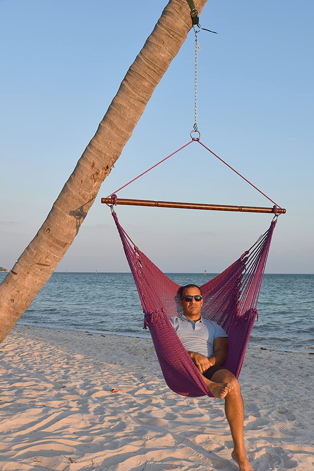 Man relaxing in a purple Jumbo Caribbean Hammock Chair hung from a leaning palm tree on a beach
