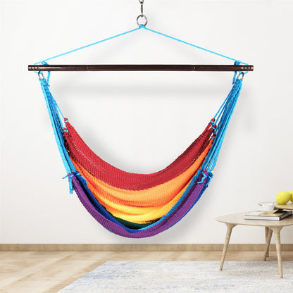 Rainbow Jumbo Caribbean Hammock Chair hanging indoors beside a small round side table against a cream wall