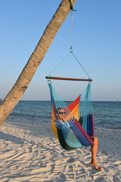 Man relaxing in a rainbow Jumbo Caribbean Hammock Chair hung from a leaning palm tree on a beach