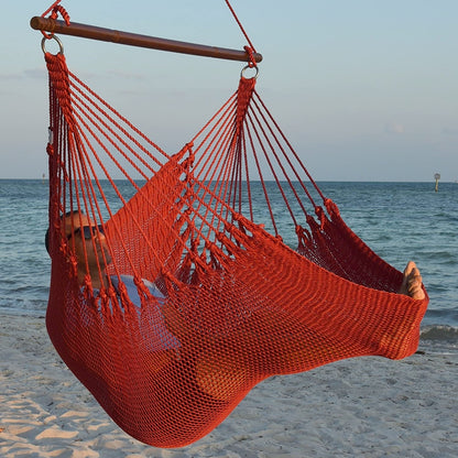 Man in sunglasses stretched out in a red Jumbo Caribbean Hammock Chair with calm ocean behind