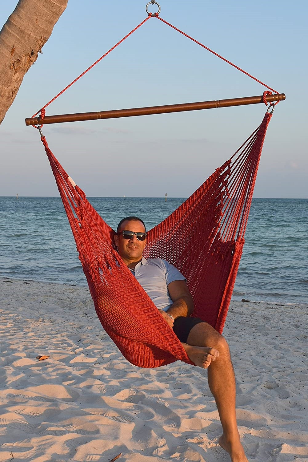 Man in sunglasses seated in a red Jumbo Caribbean Hammock Chair on a white sand beach