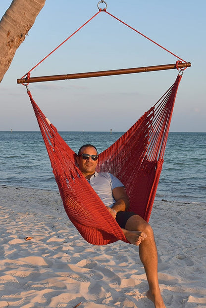 Man in sunglasses seated in a red Jumbo Caribbean Hammock Chair on a white sand beach