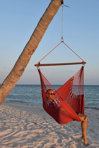 Man relaxing in a red Jumbo Caribbean Hammock Chair hung from a leaning palm tree on a beach