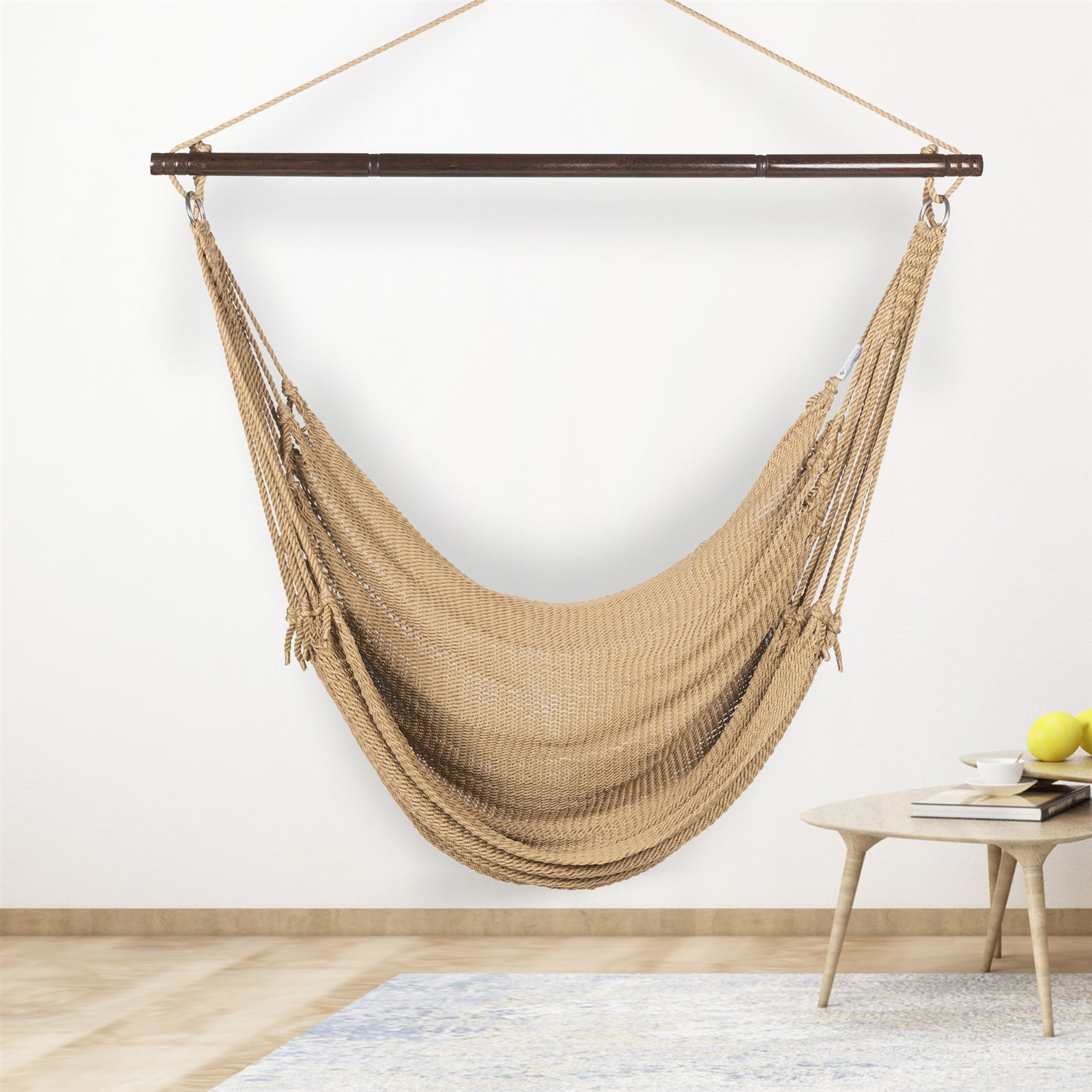 Tan Jumbo Caribbean Hammock Chair hanging indoors beside a small round side table against a cream wall