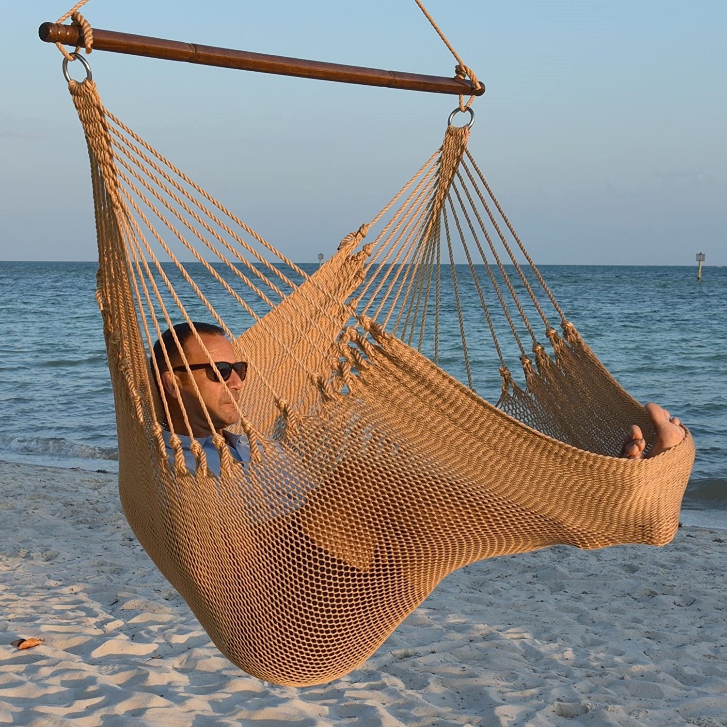 Man in sunglasses stretched out in a tan Jumbo Caribbean Hammock Chair with calm ocean behind