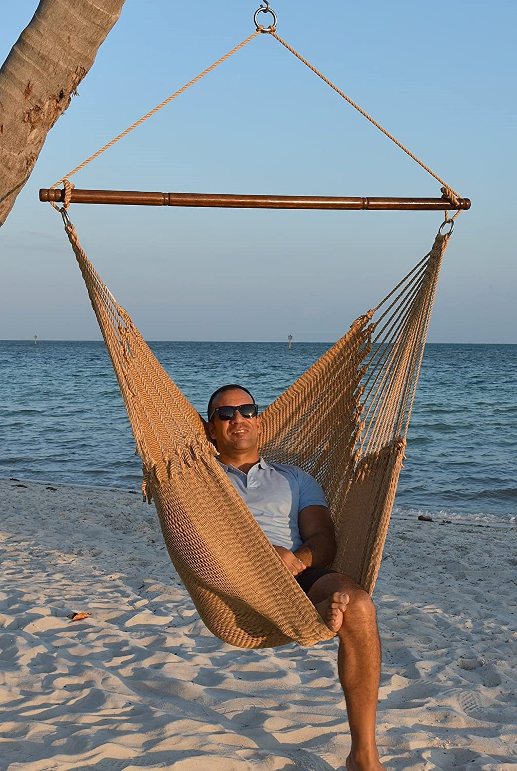 Man in sunglasses seated in a tan Jumbo Caribbean Hammock Chair on a white sand beach