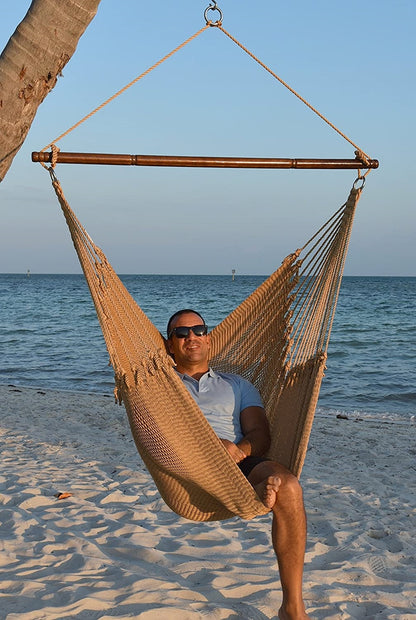 Man in sunglasses seated in a tan Jumbo Caribbean Hammock Chair on a white sand beach