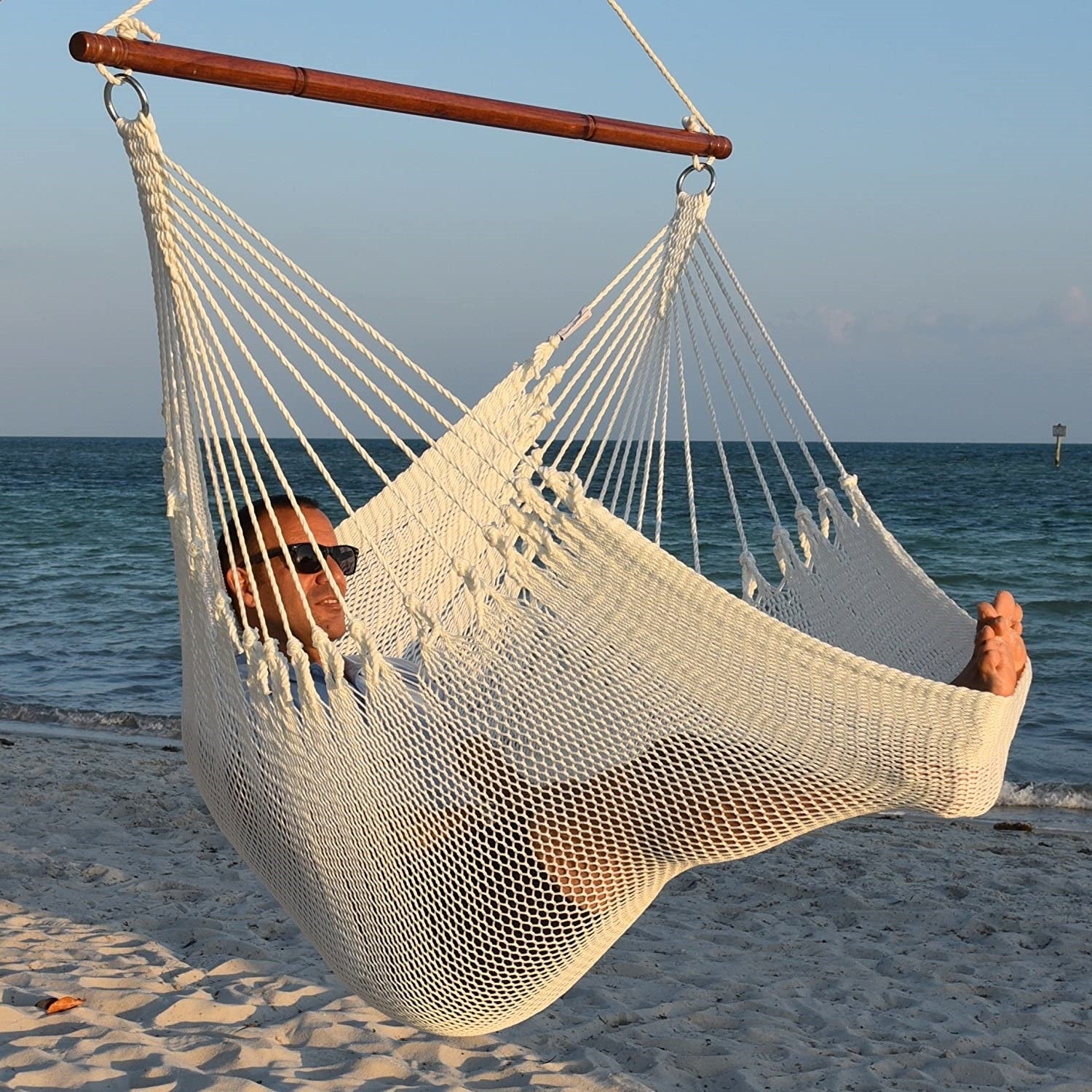 Man in sunglasses stretched out in a white Jumbo Caribbean Hammock Chair with calm ocean behind