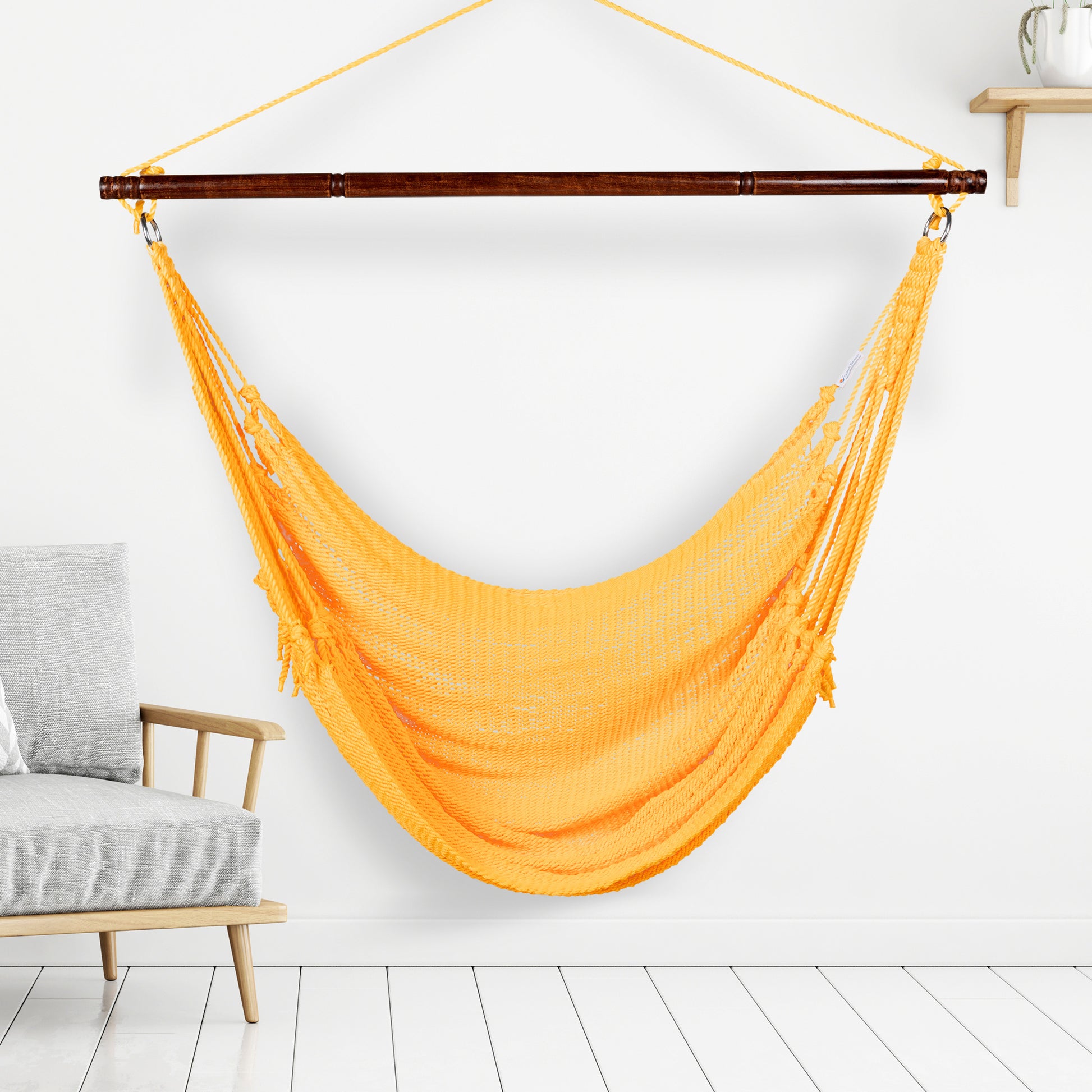 Yellow Jumbo Caribbean Hammock Chair hanging indoors beside a pale wood armchair against a white wall